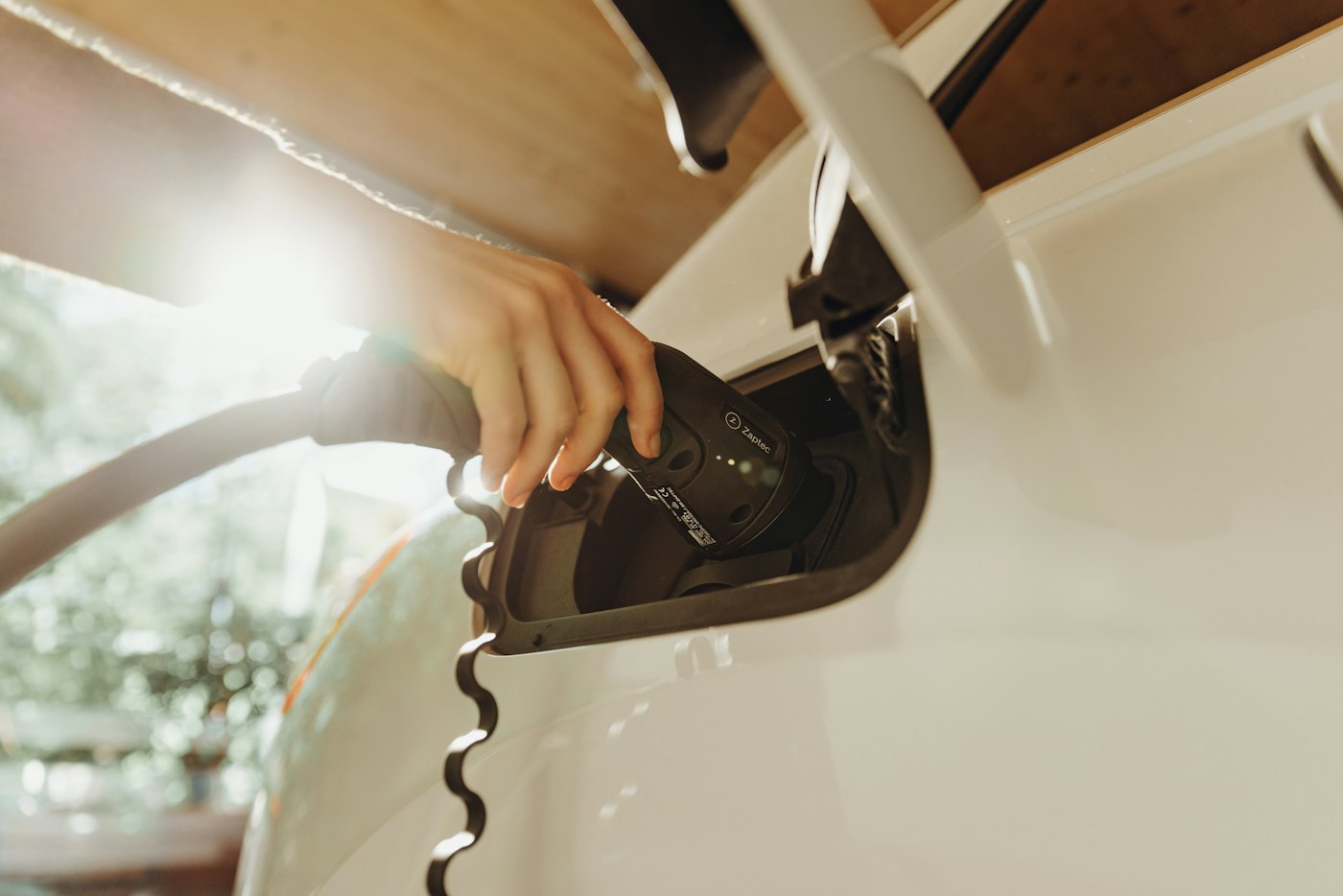 A hand plugging a charging cable into the port of a white electric vehicle
