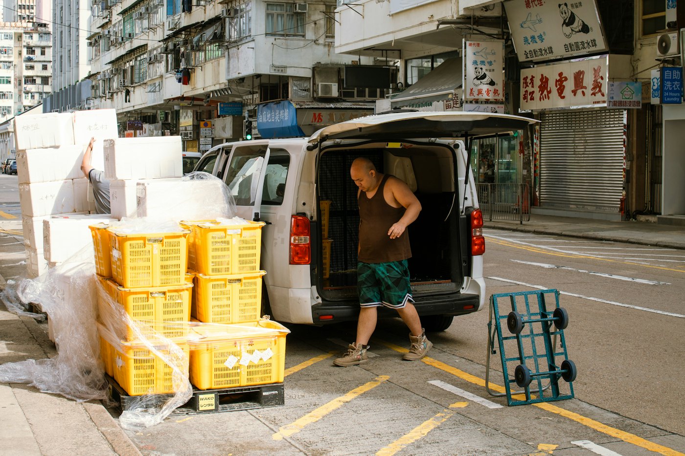A man lifting stacked crates out of the back of a van at the kerbside