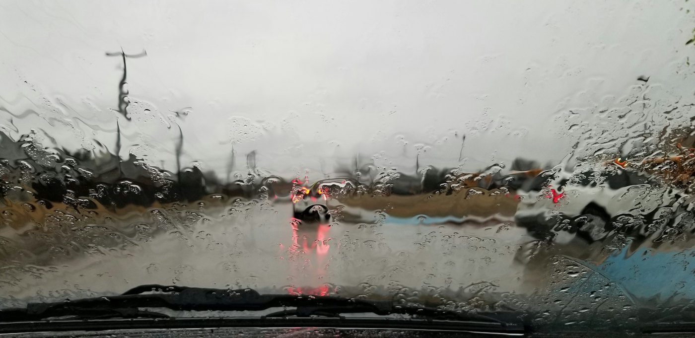 A vehicle on a road in heavy rain, spray coming off the surface